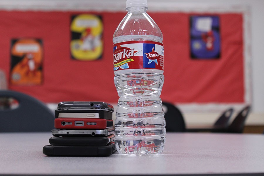 A stack of cellphones next to one water bottle, visually showing that people will be more smartphones than running water. In the year 2020 it is estimated that people will have more phones than water.