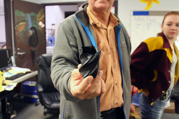 Wasson holds a 3D printed spiral, demonstrating the 3D printer's capabilities. The black filament indicates it was printer on Wasson's home printer.