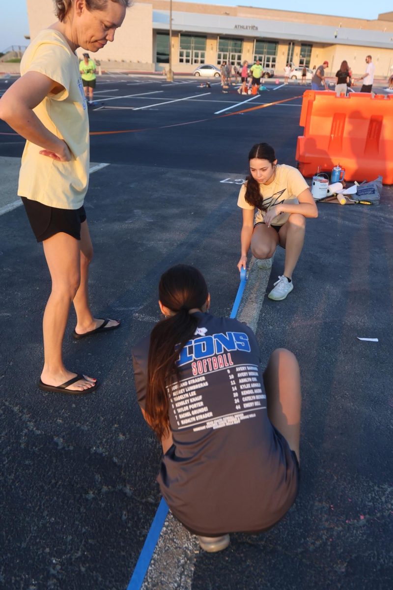Maddie Lee holds down tape while her sister Meagan helps put borders on the spot. Their mother, Leslie, also helped paint spot F67. Maddie said they got there so early "before it gets too hot." Seniors painted their parking spots both in front of and behind the school on Saturday, Aug. 9.
