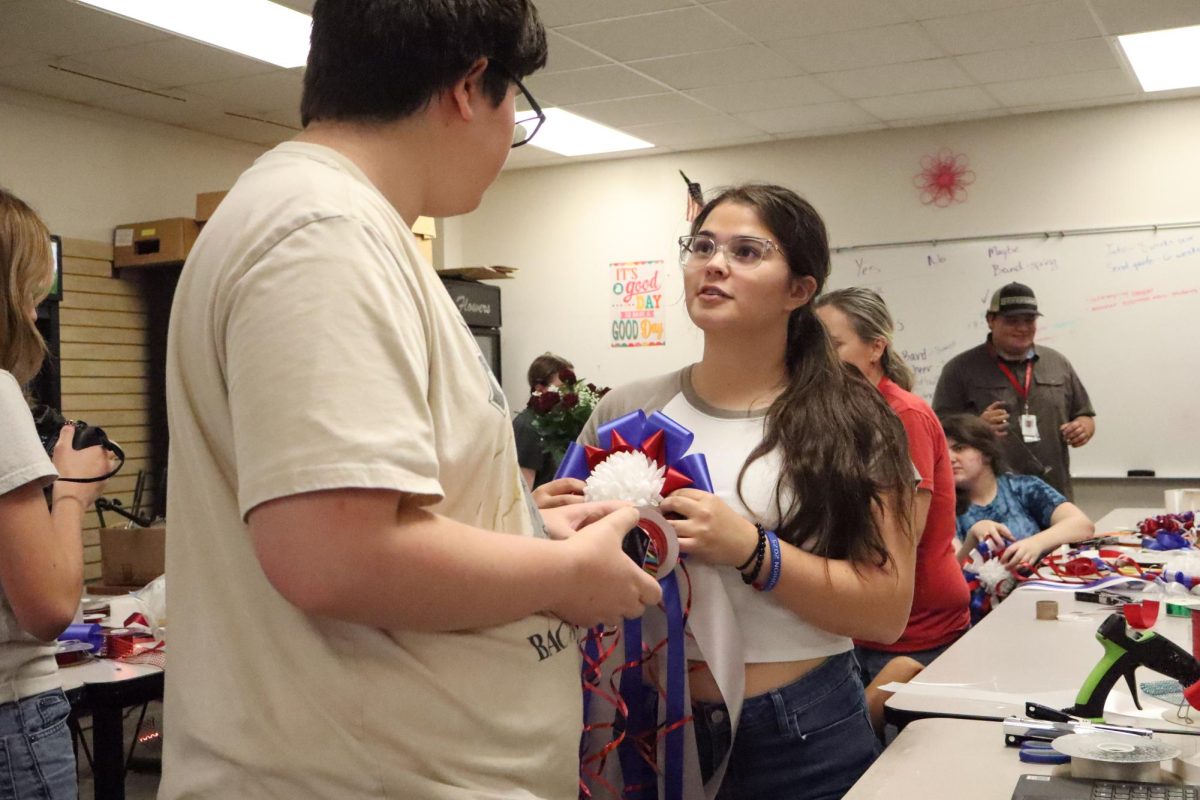Junior Addisen Burnet assisting freshman Lucas Challis in making a mum during floral design class in CTE building on Sept. 23.