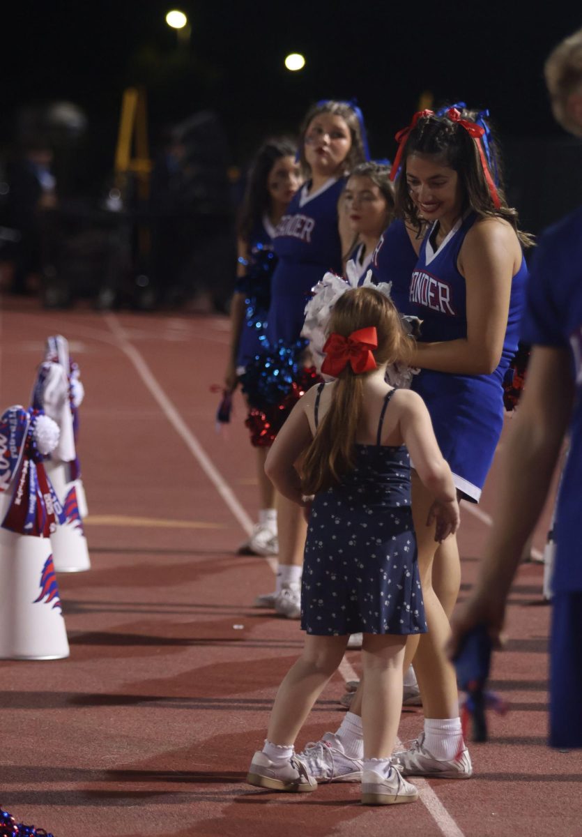 On the sidelines, junior Hailey Wust answers a young girl's questions about cheer.