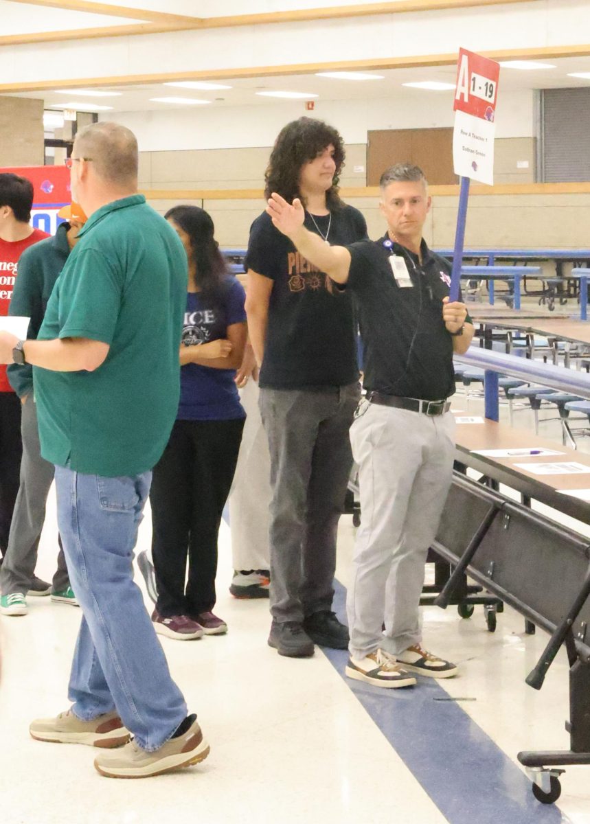 Waving his hand out to create directions, assistant principal Dessard Norris helps assistant principal Devin Eatmon lead students by their last names as part of the graduation practice held in the dance gym and cafeteria May 28.