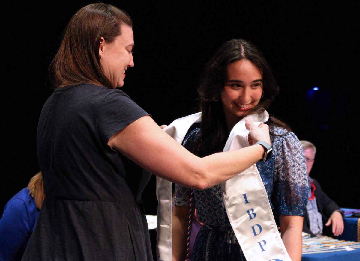 IB teacher Kate Haunstein gives Senior Zina Baker International Baccalaureate sash at senior awards ceremony in the performing arts center May 20.