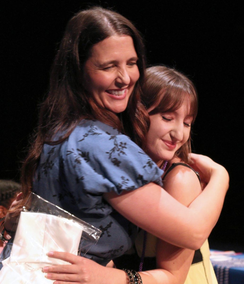 Senior Zoe Effenberger and dual credit coordinator Megan Wolske hug on stage at senior awards ceremony in the performing arts center May 20.